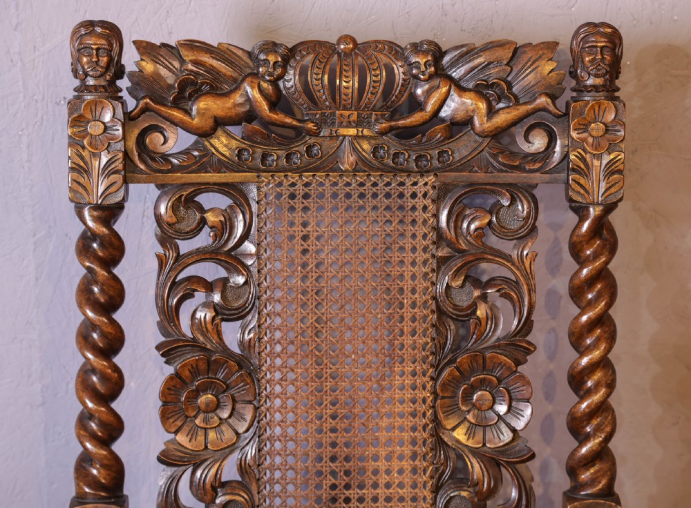 Set of six high-backed Carolean style walnut dining chairs featuring intricate scroll and crown carvings, barley twist pillars, cane back panels, and blue velvet upholstered seats. View XVII