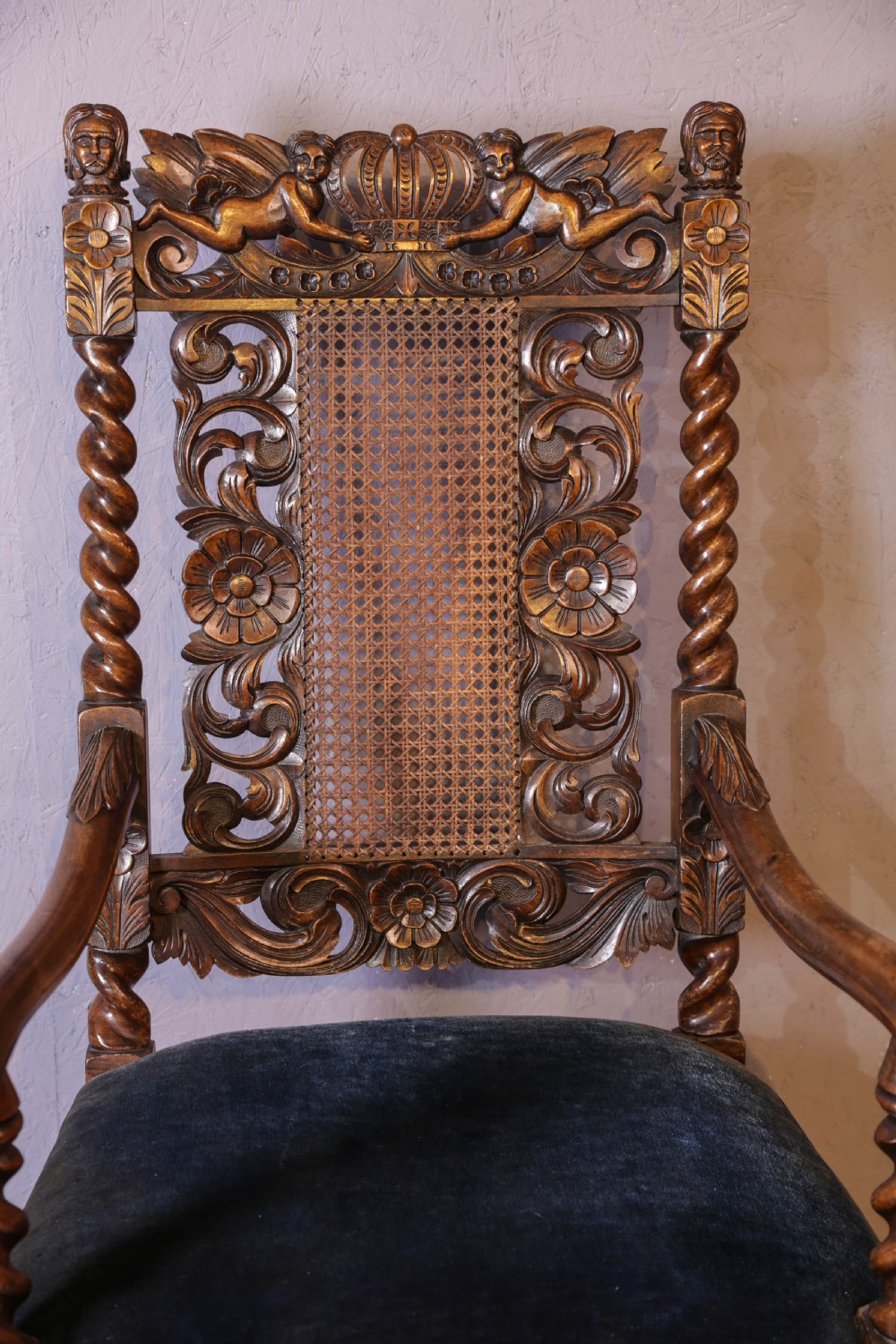 Set of six high-backed Carolean style walnut dining chairs featuring intricate scroll and crown carvings, barley twist pillars, cane back panels, and blue velvet upholstered seats. View XVIII