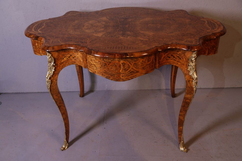 A French Rococo Revival centre table featuring burr walnut marquetry, a serpentine top, cabriole legs, and ornate gilt-bronze mounts.