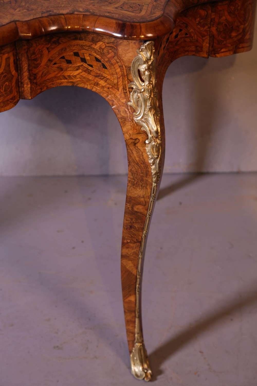 A French Rococo Revival centre table featuring burr walnut marquetry, a serpentine top, cabriole legs, and ornate gilt-bronze mounts. View IV