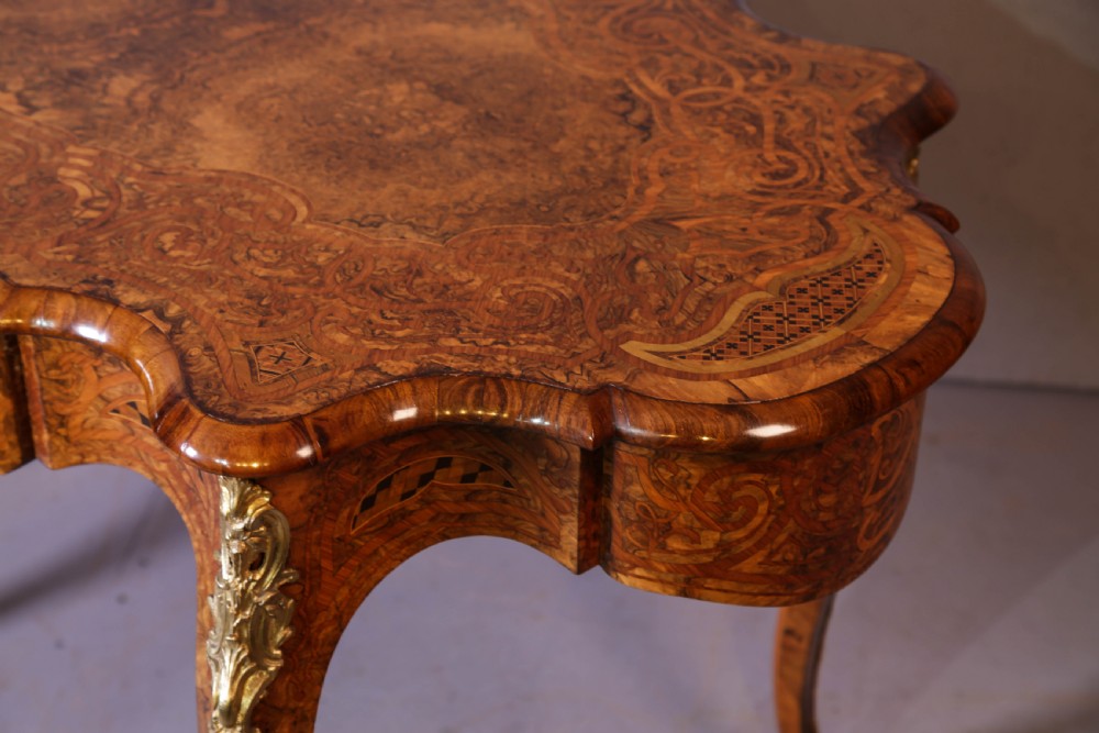 A French Rococo Revival centre table featuring burr walnut marquetry, a serpentine top, cabriole legs, and ornate gilt-bronze mounts. View V