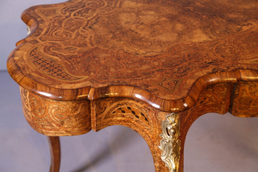 A French Rococo Revival centre table featuring burr walnut marquetry, a serpentine top, cabriole legs, and ornate gilt-bronze mounts. View VI