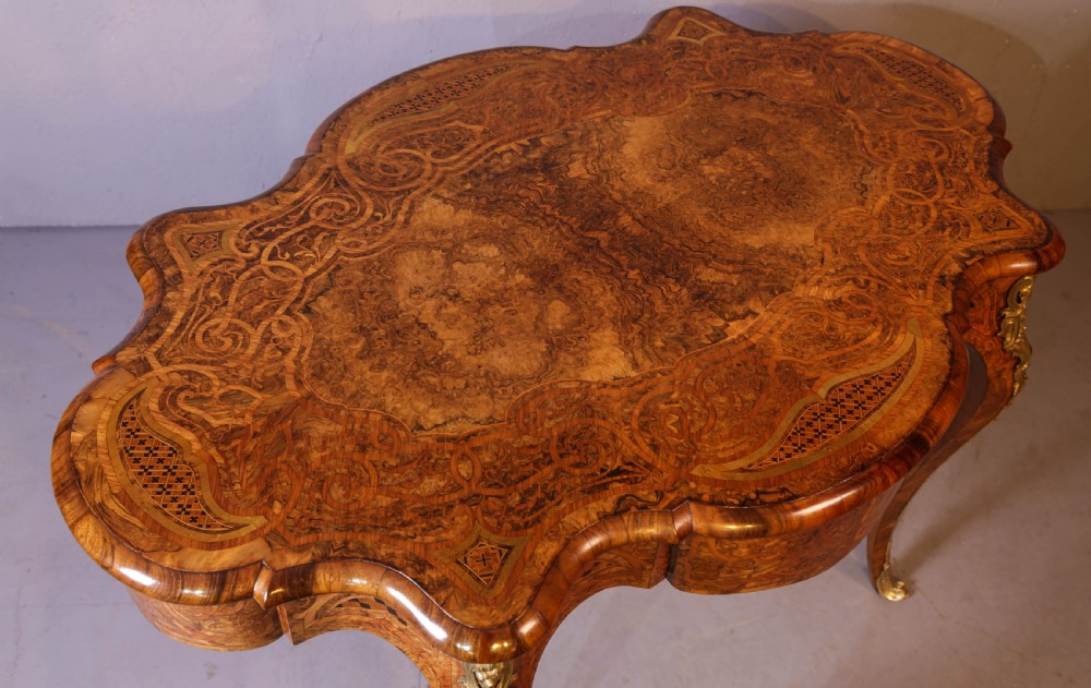 A French Rococo Revival centre table featuring burr walnut marquetry, a serpentine top, cabriole legs, and ornate gilt-bronze mounts. View X