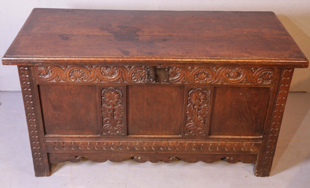 A 17th century carved oak coffer featuring a three-panel front with hand-carved leaf motifs, lunette top frieze, and iron lock plate.