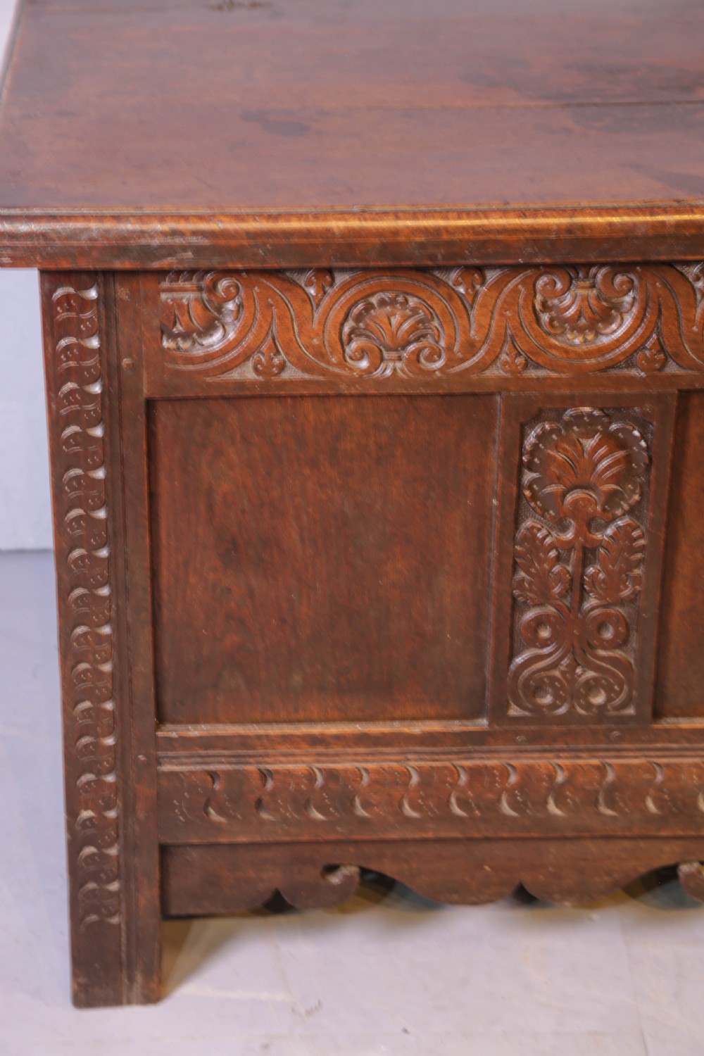 A 17th century carved oak coffer featuring a three-panel front with hand-carved leaf motifs, lunette top frieze, and iron lock plate. View V