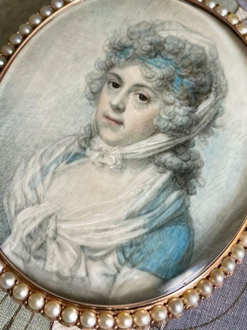 fig 2. An oval Georgian portrait miniature depicting a woman with curled hair in a blue dress, enclosed within a pearl-set frame.