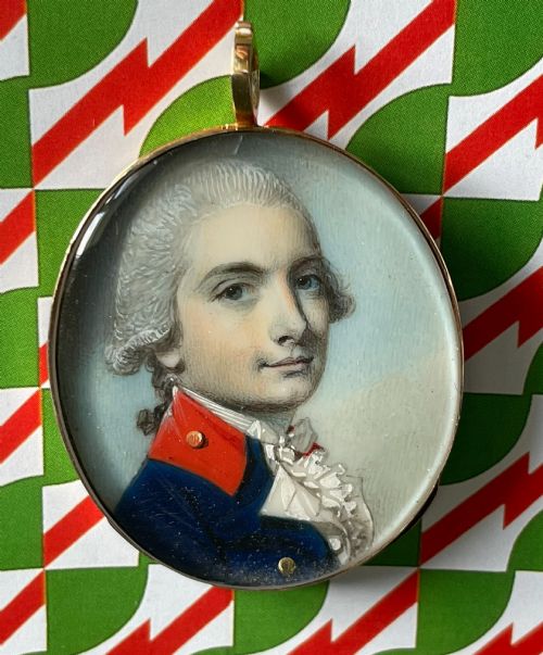 fig 1. An oval Georgian portrait miniature depicting a young officer in a blue uniform coat with red collar facings, mounted in a gold pendant casing.