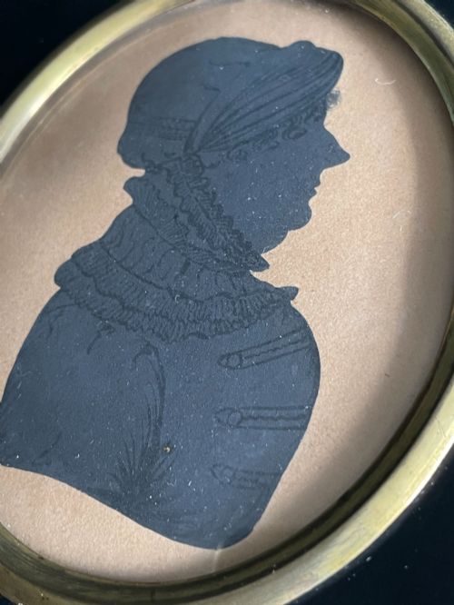 fig 1. A profile silhouette portrait enclosed in an oval brass bezel and mounted within a rectangular black ebonised frame featuring a brass acorn hanger.