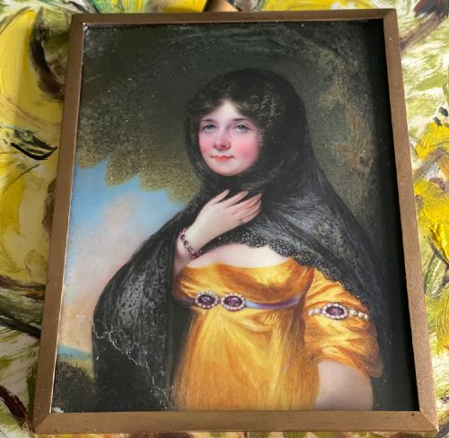 fig 2. A Georgian enamel portrait miniature depicting a woman in a yellow gown and black lace head covering, presented in a metal frame with a top loop.