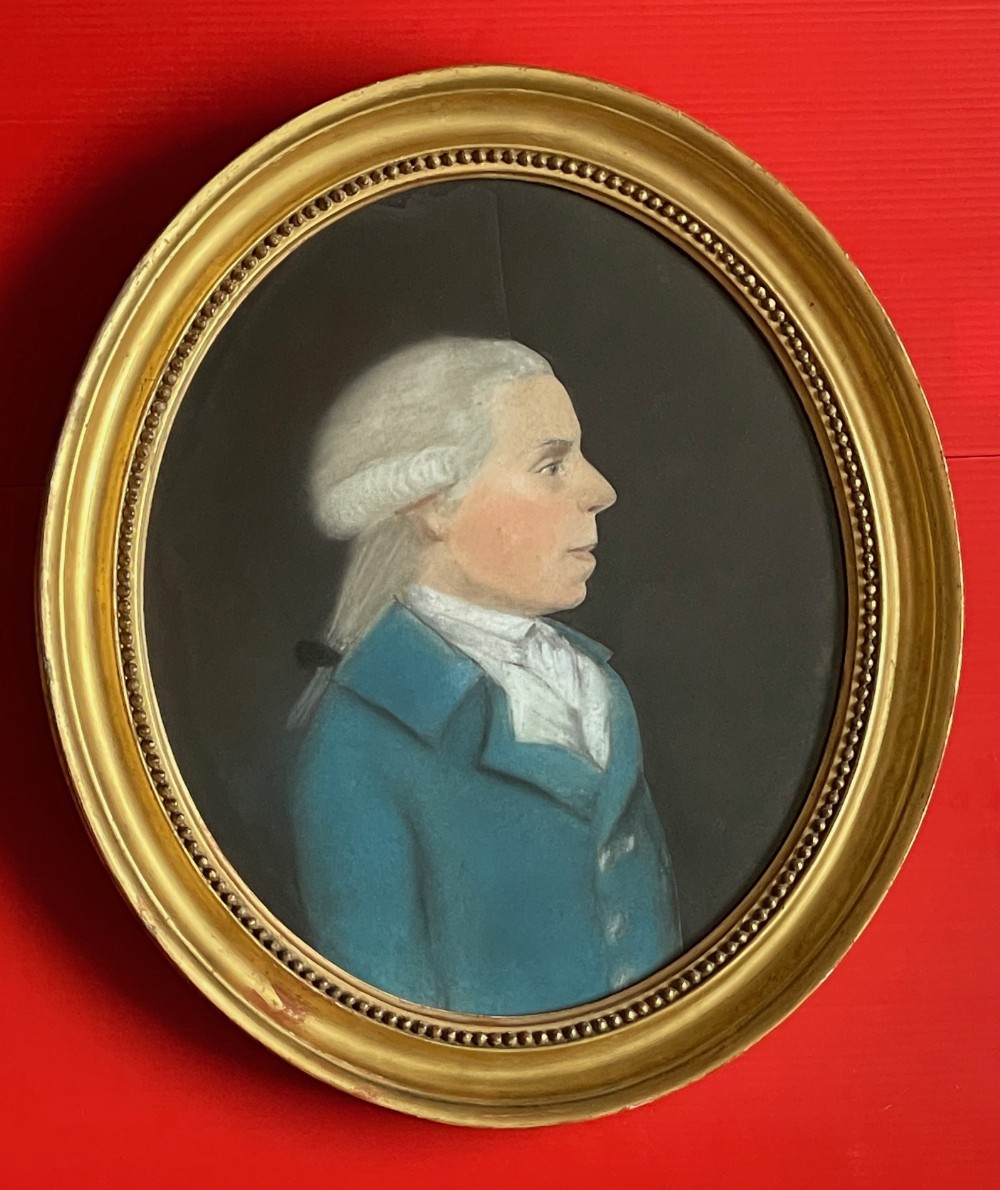 An 18th-century oval pastel profile portrait of a gentleman wearing a blue coat and powdered wig, enclosed in a beaded gilt frame.