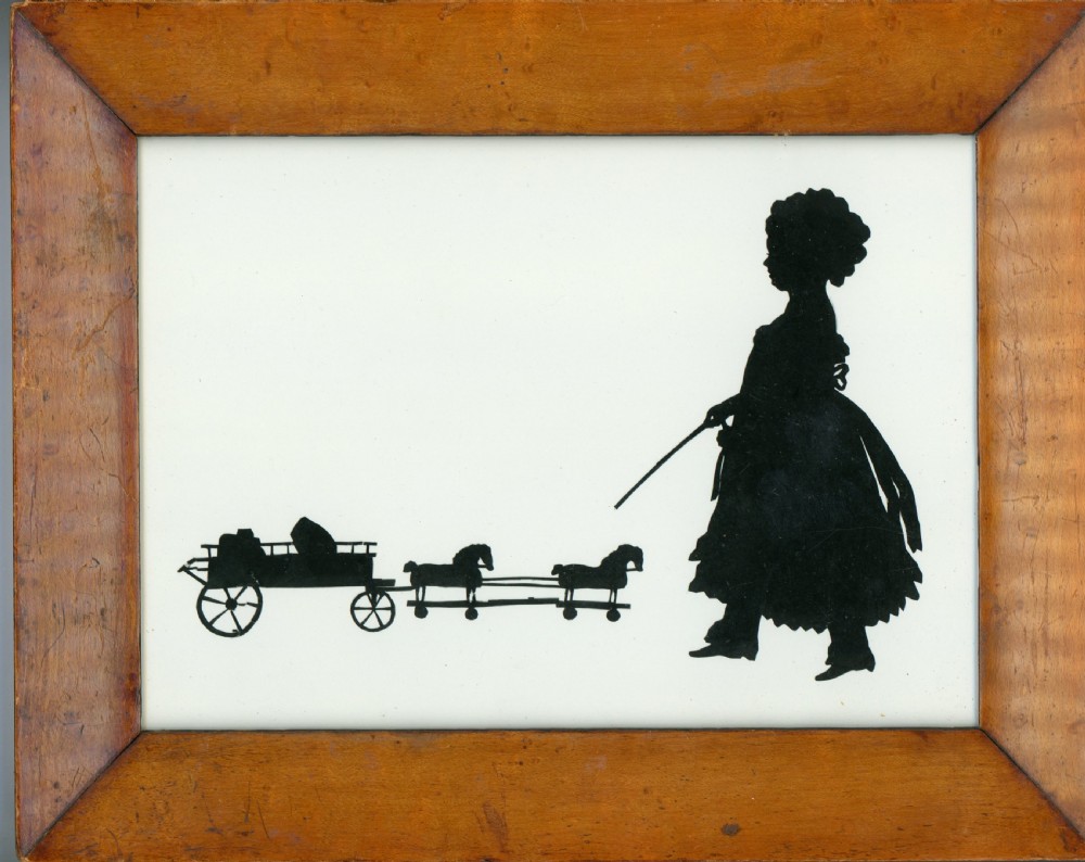 A framed 19th-century black paper cut silhouette depicting a child pulling a toy horse cart against an off-white background.