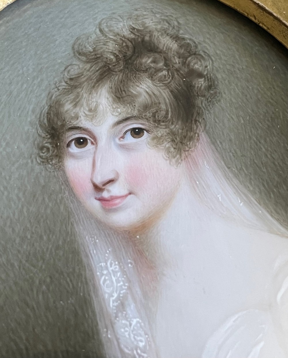 An oval watercolour miniature portrait depicting a woman with dark eyes, curled brown hair, and a translucent veil against a hatched grey background.