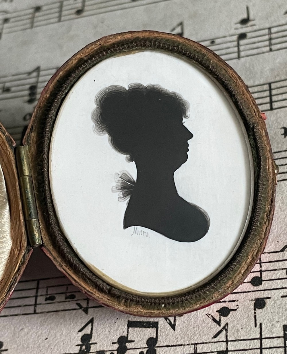 An oval Georgian profile silhouette portrait of a woman in black ink set inside a hinged leather case.