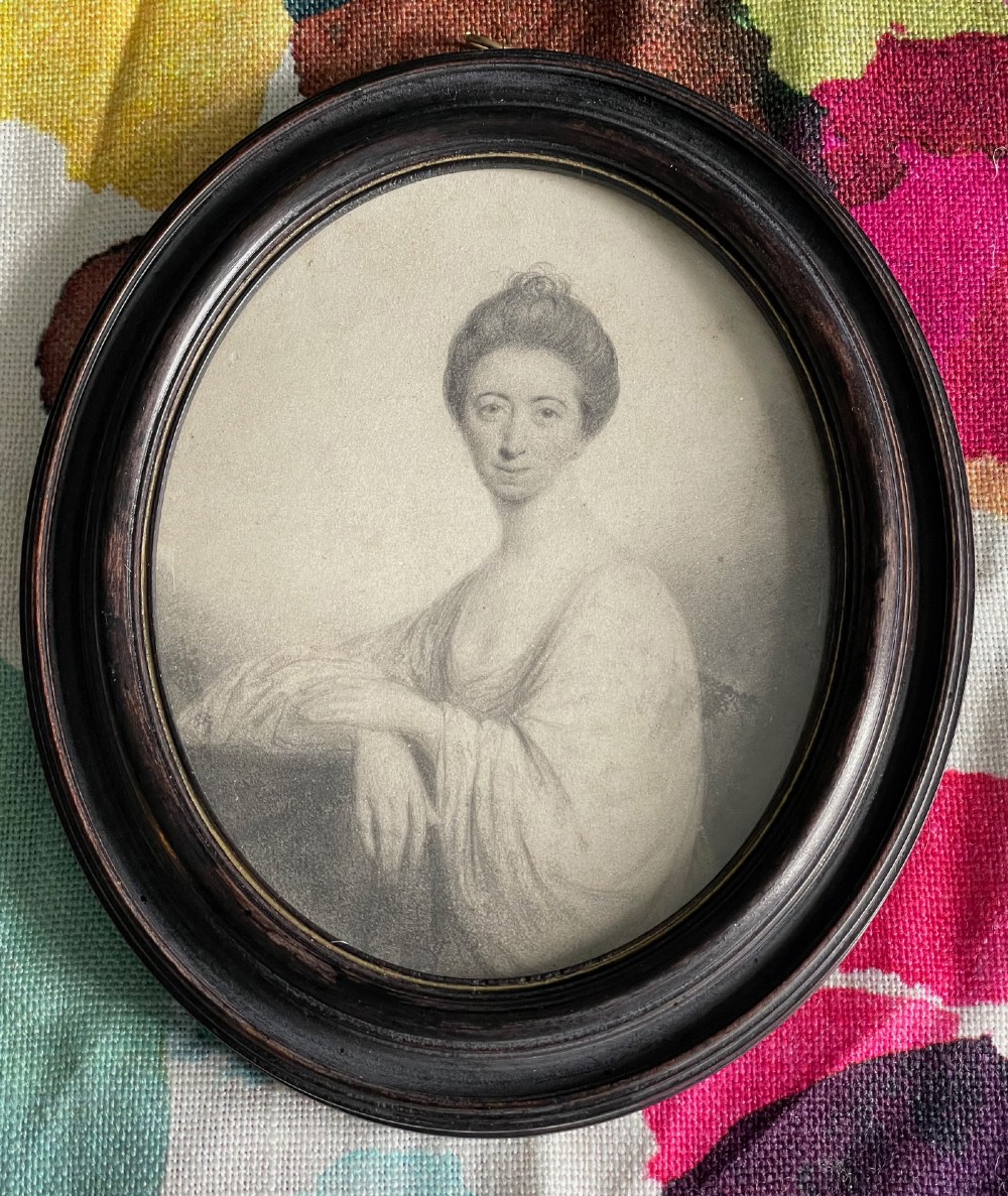 An 18th-century oval monochrome plumbago portrait drawing of a woman, housed in a dark turned wooden frame.