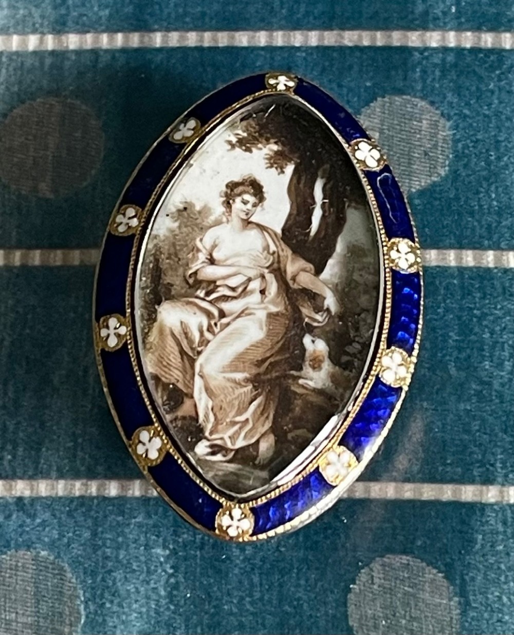 An oval Georgian brooch featuring a hand-painted sepia miniature portrait enclosed within a royal blue vitreous enamel border with white floral accents.
