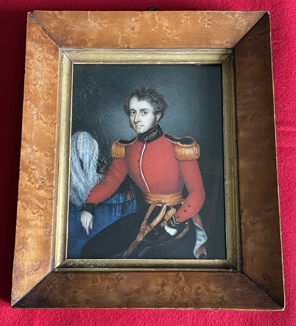 An antique portrait miniature depicting a Dragoon officer in a red uniform with gold epaulettes, housed in a burl wood frame with a gilt inner sight edge.