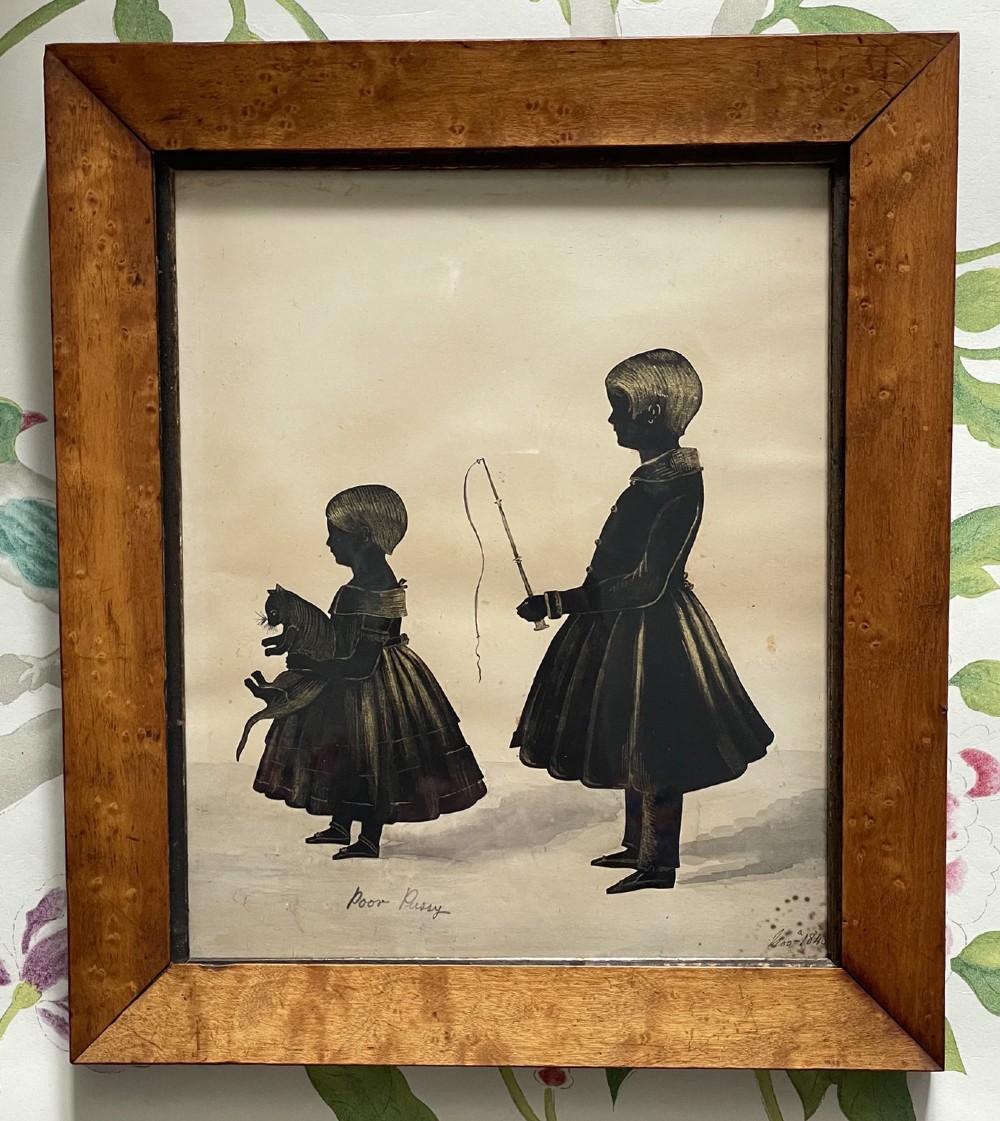 A framed 1846 Victorian cut-paper silhouette depicting two children and a cat, rendered in black ink with gold bronzing details inside a bevelled birdseye maple wood frame.
