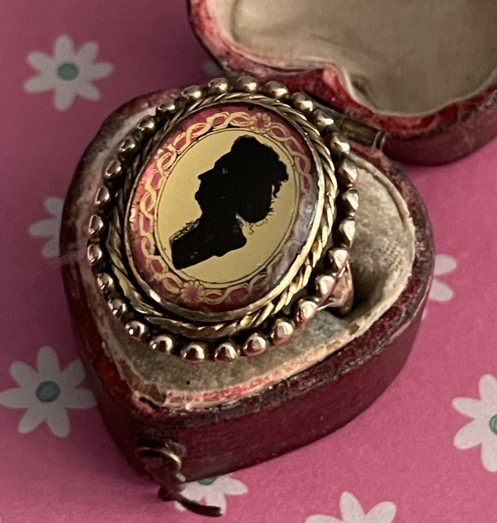 An antique Georgian oval ring featuring a reverse-painted verre eglomise silhouette portrait set within a beaded gold bezel.