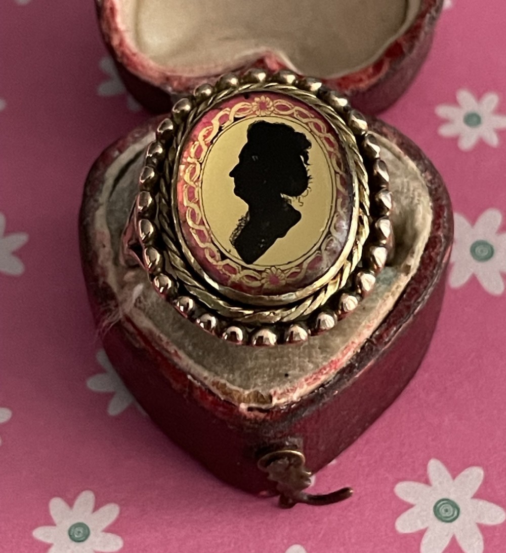 An antique Georgian oval ring featuring a reverse-painted verre eglomise silhouette portrait set within a beaded gold bezel. View X