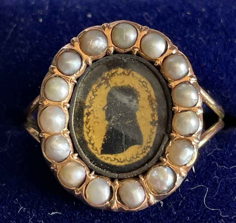 An oval Georgian gold ring featuring a miniature silhouette portrait set beneath glass and framed by a halo of split pearls.