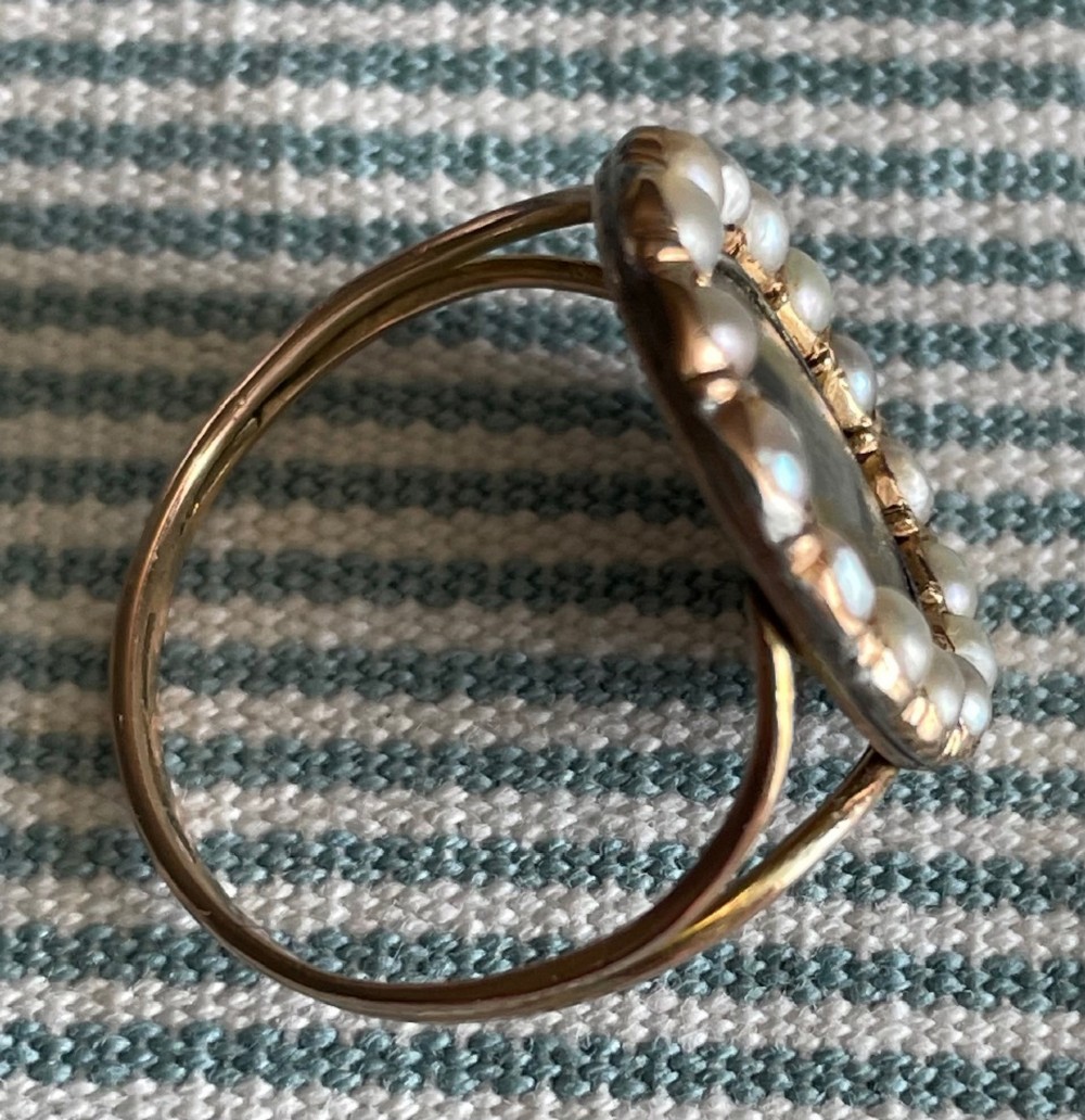 An oval Georgian gold ring featuring a miniature silhouette portrait set beneath glass and framed by a halo of split pearls. View II