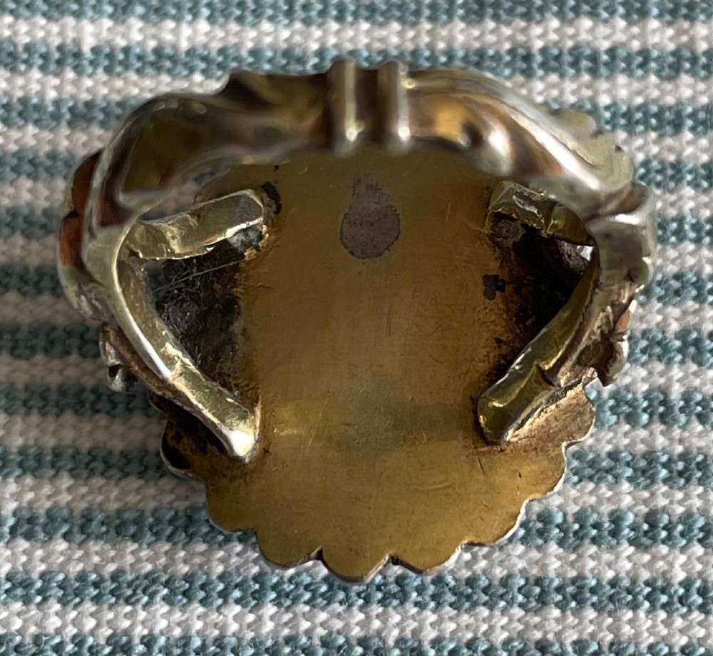 An oval antique Georgian silver ring featuring a black silhouette profile portrait of a figure wearing a hat set over a gold foil background within a crimped silver bezel. View III