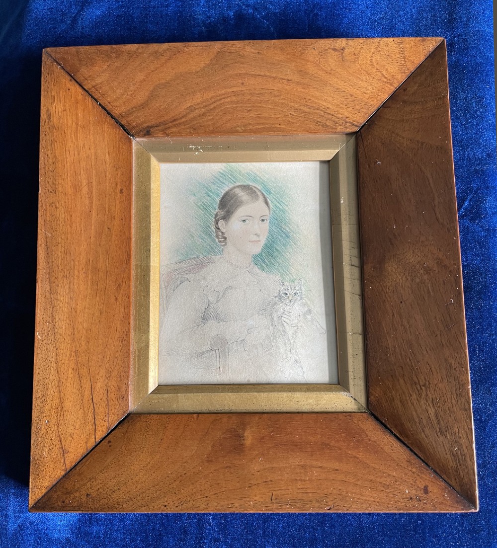 A framed 19th-century pencil and watercolour portrait depicting a seated woman holding a cat, set within a wide bevelled wooden frame with a gilt inner liner.