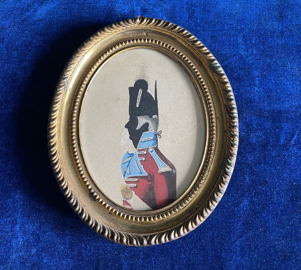 An oval giltwood frame displaying a hand-painted profile portrait silhouette of a military officer in a red uniform coat.