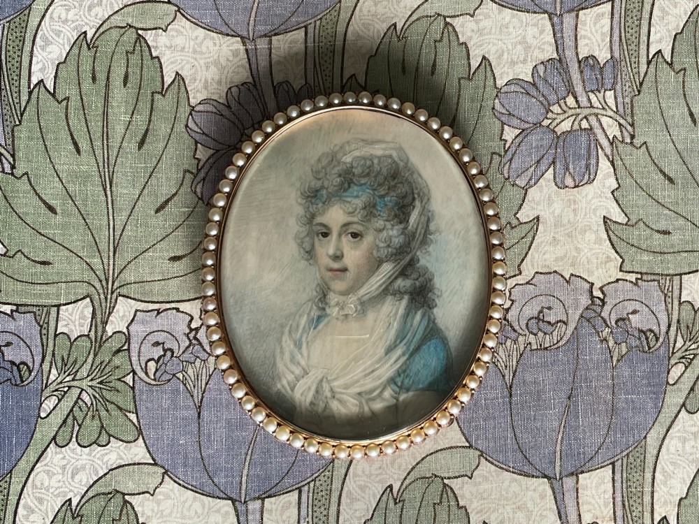 An oval Georgian portrait miniature depicting a woman with curled hair in a blue dress, enclosed within a pearl-set frame.