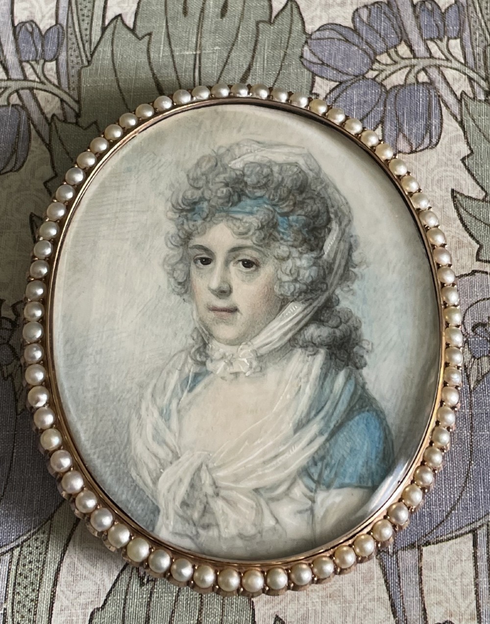 An oval Georgian portrait miniature depicting a woman with curled hair in a blue dress, enclosed within a pearl-set frame. View II