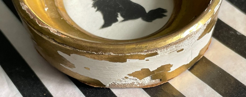 A miniature black cut-paper silhouette depicting a seated dog profile within a deep, oval giltwood frame. View II