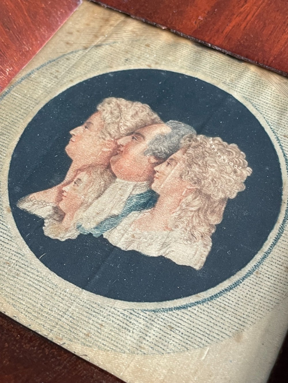 An antique silk print depicting profile portraits of Louis XVI and his family inside a circular medallion, enclosed within a deep square mahogany frame. View VII