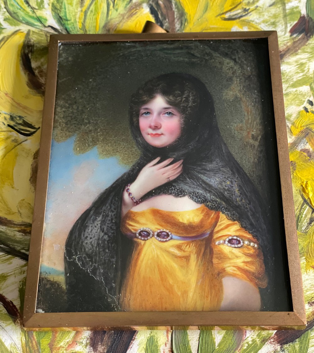 A Georgian enamel portrait miniature depicting a woman in a yellow gown and black lace head covering, presented in a metal frame with a top loop. View II