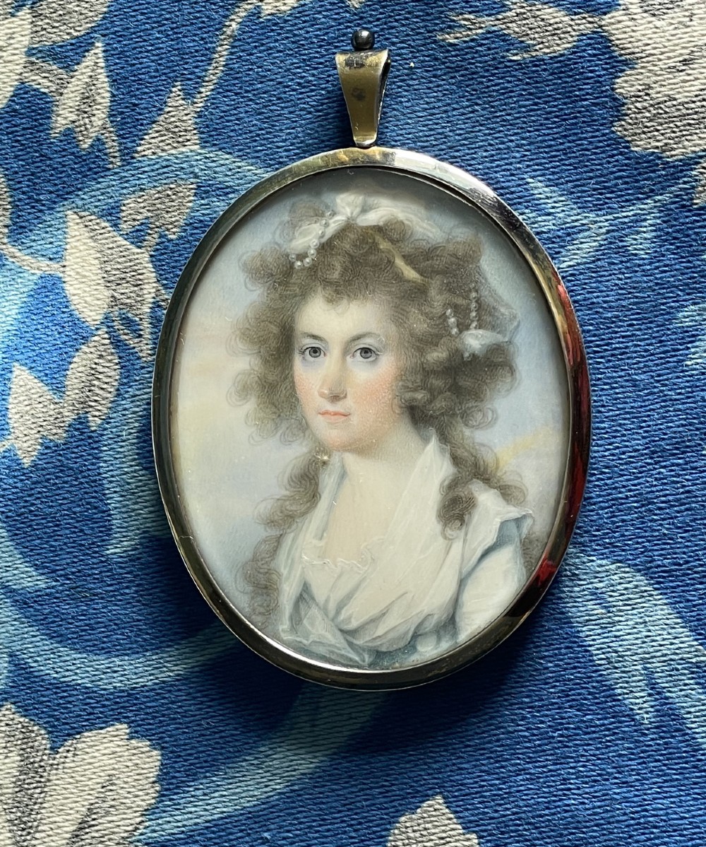 An oval Georgian portrait miniature of a lady with powdered curls set within a gold pendant frame.