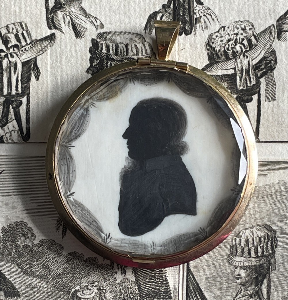 A circular double-sided Georgian silhouette portrait pendant showing two profile portraits painted in black pigment. View III