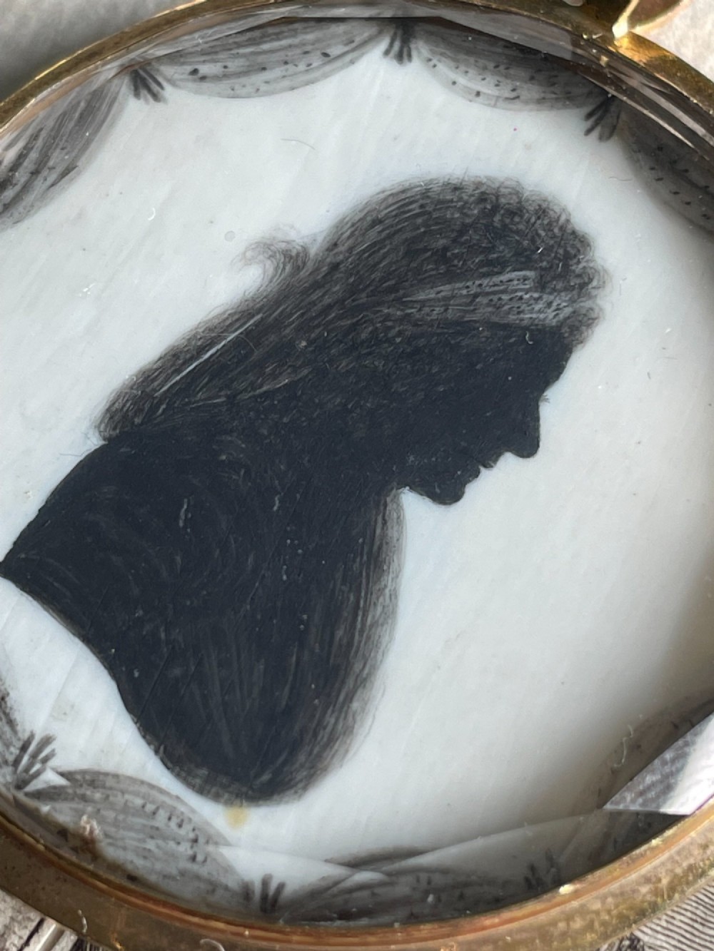 A circular double-sided Georgian silhouette portrait pendant showing two profile portraits painted in black pigment. View IV
