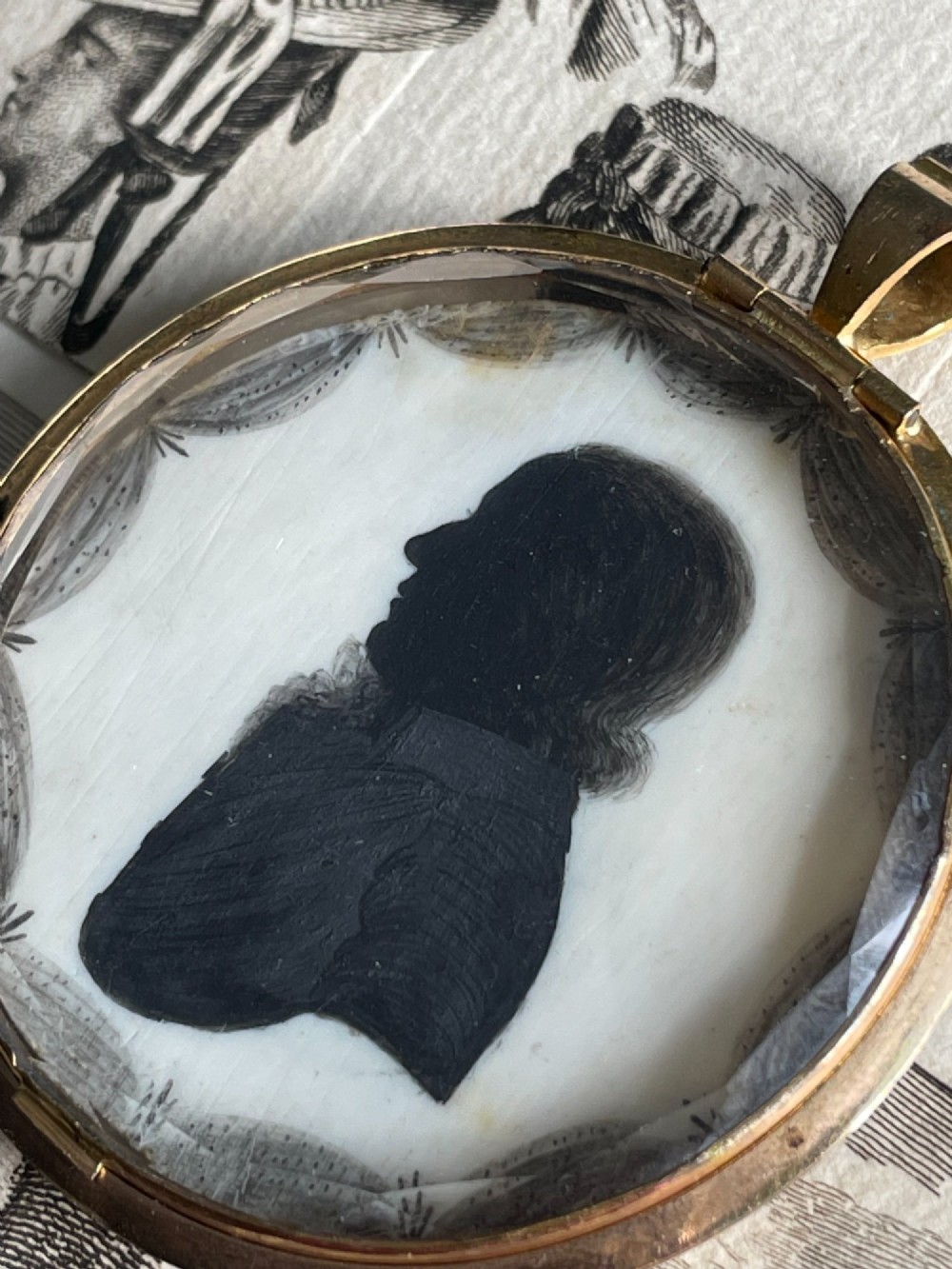 A circular double-sided Georgian silhouette portrait pendant showing two profile portraits painted in black pigment. View V