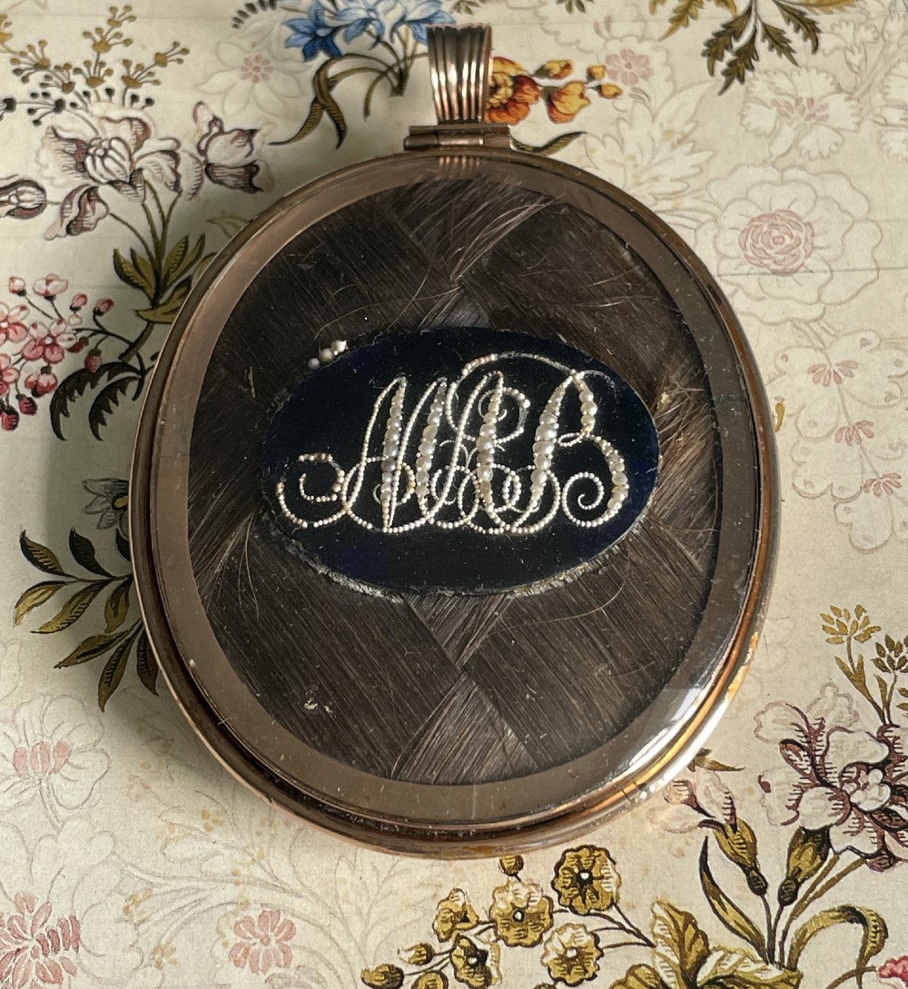An oval Regency portrait miniature depicting a woman with dark hair in an updo wearing a white high-waisted gown, mounted in a gold casing with a ribbed loop. View II