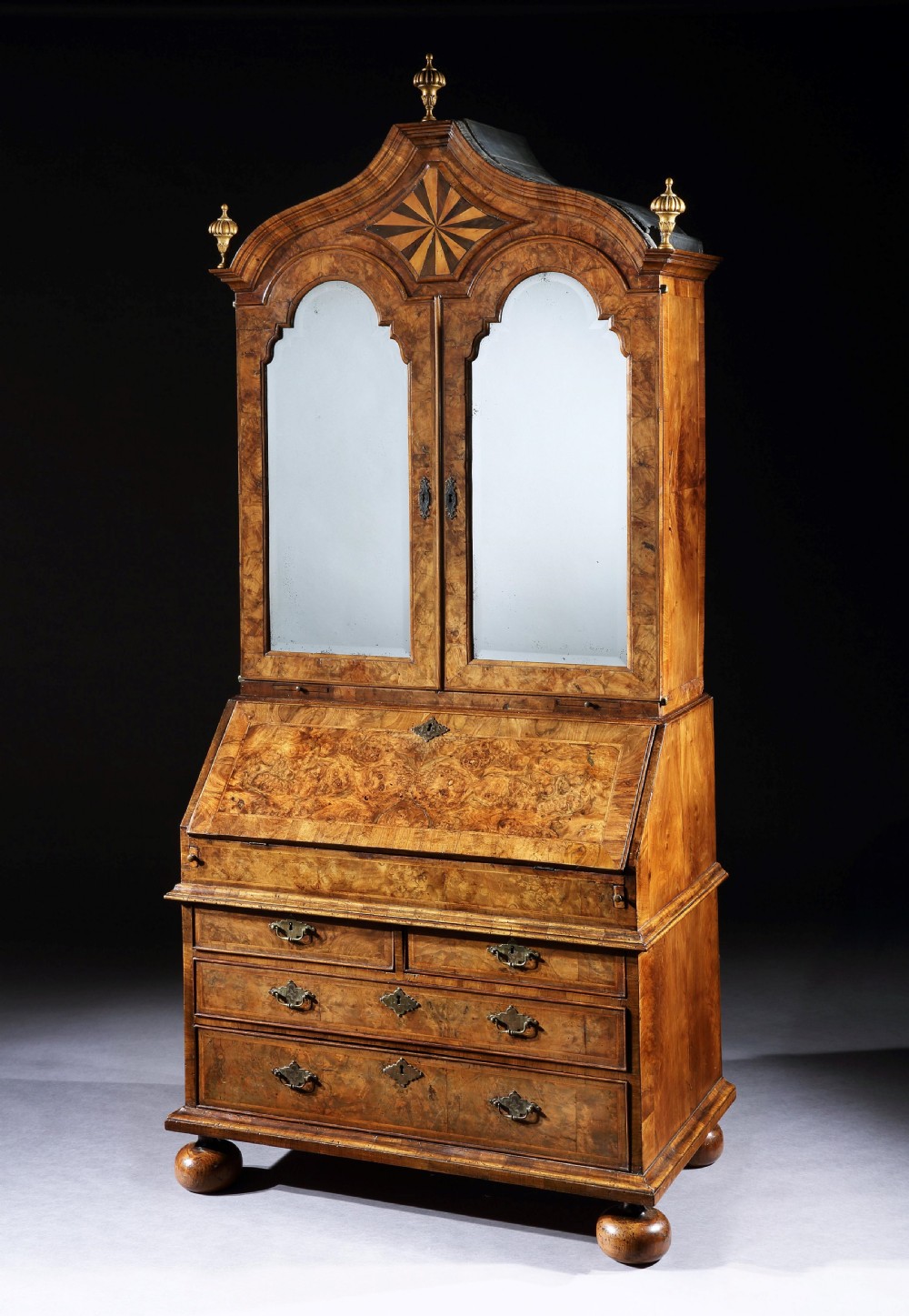 An antique William & Mary walnut bureau bookcase featuring a double-arched upper section with mirrored doors, a slant-front writing desk, and graduated drawers on ball feet.