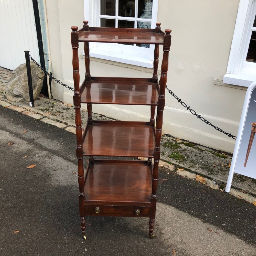 A four-tiered Regency mahogany whatnot featuring turned column supports, top corner finials, a lower drawer, and brass castors.