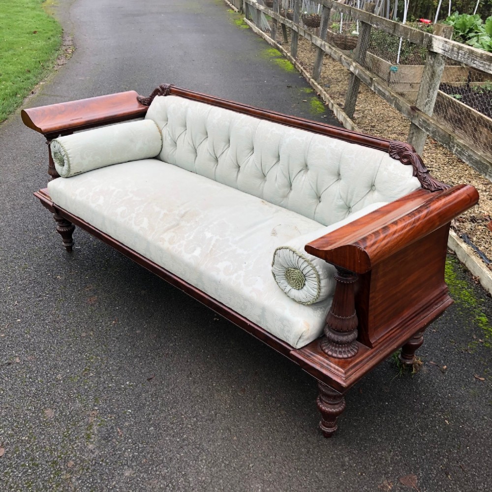 A mid 19th-century Continental mahogany settee featuring wide scroll arms, turned carved support columns, button-tufted pale green upholstery, and cylindrical bolster cushions.