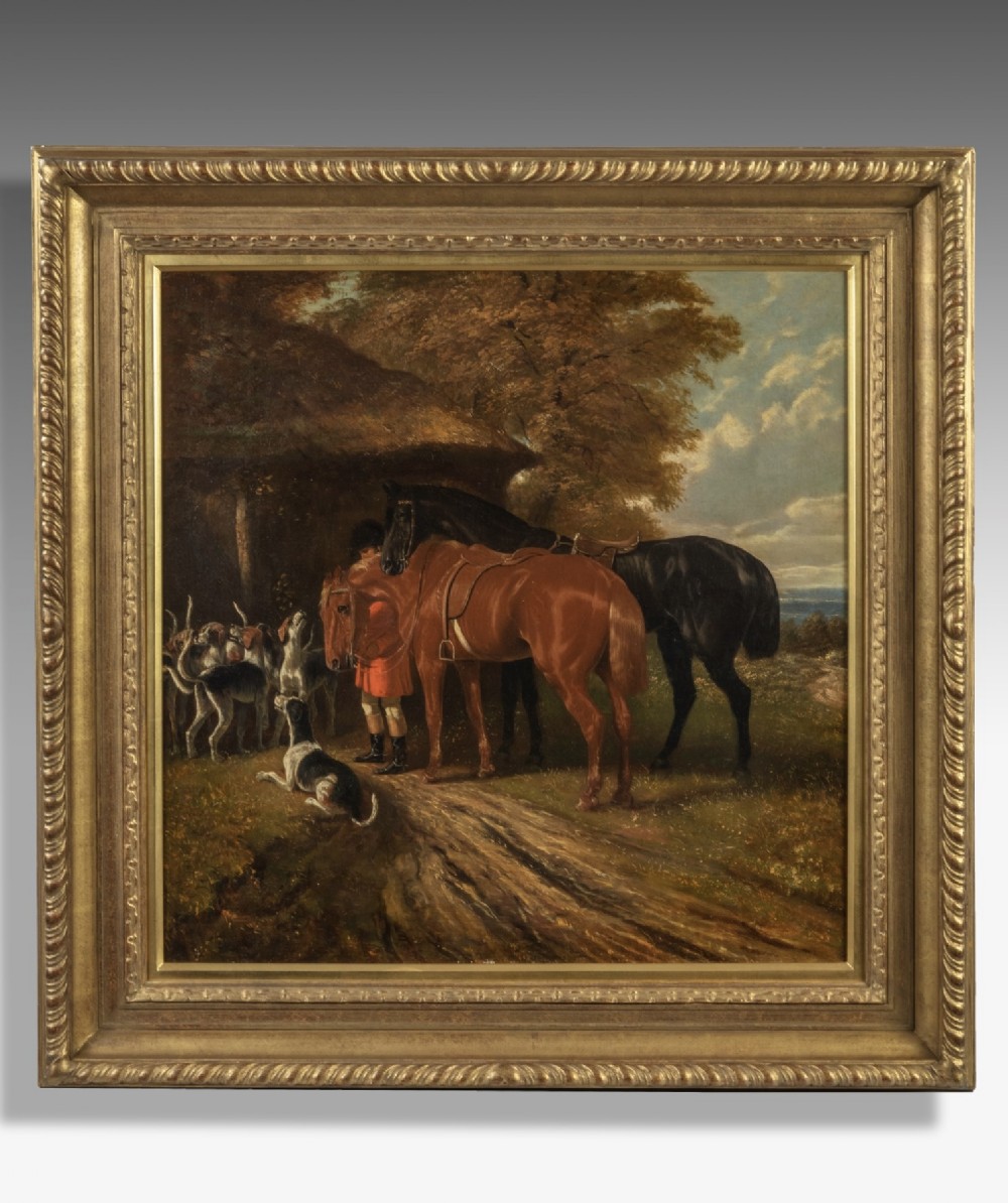 A nineteenth-century oil painting in a giltwood frame depicting two horses, foxhounds, and a huntsman beside a thatched cottage.