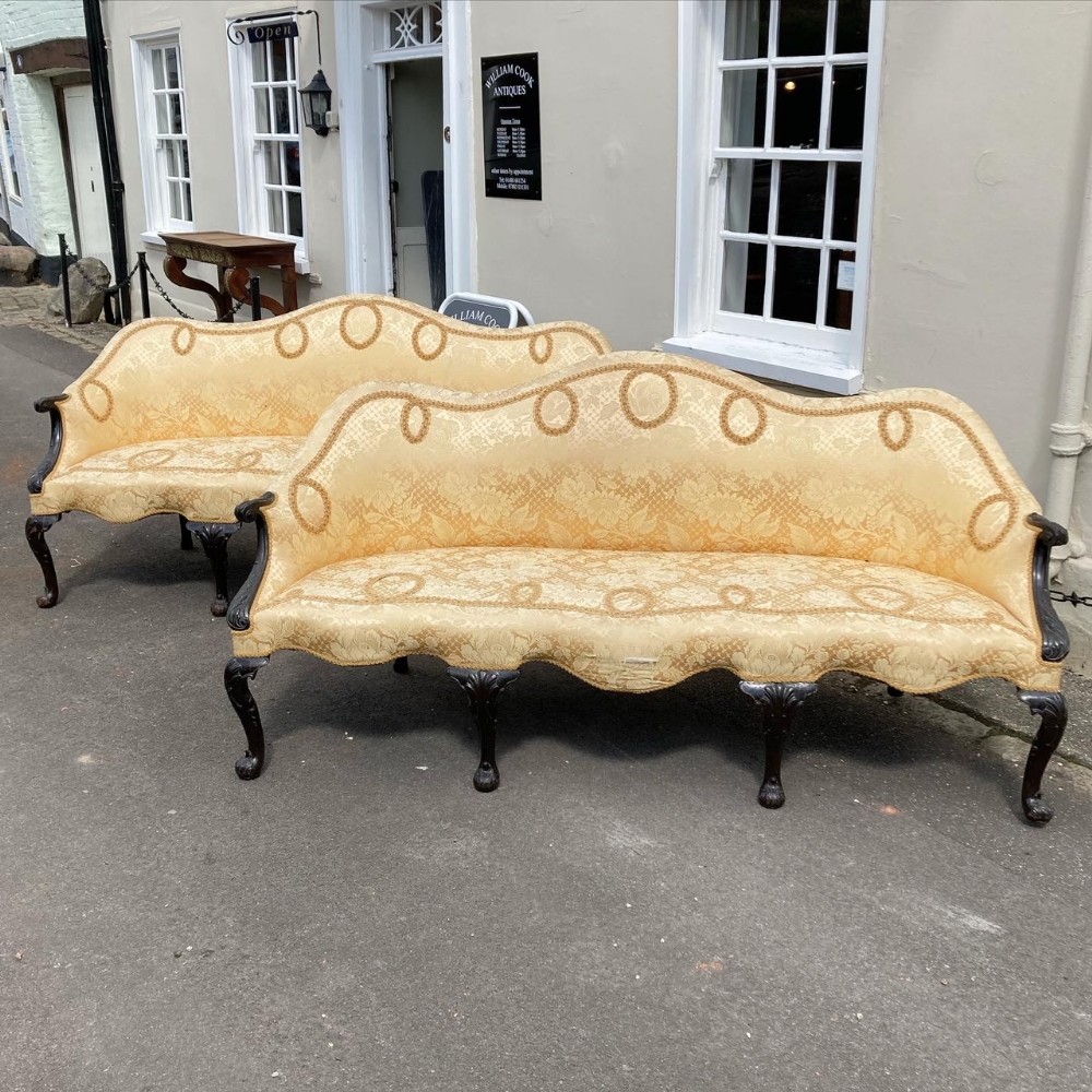 A pair of 19th-century camelback settees upholstered in patterned gold damask fabric with dark carved mahogany cabriole legs.