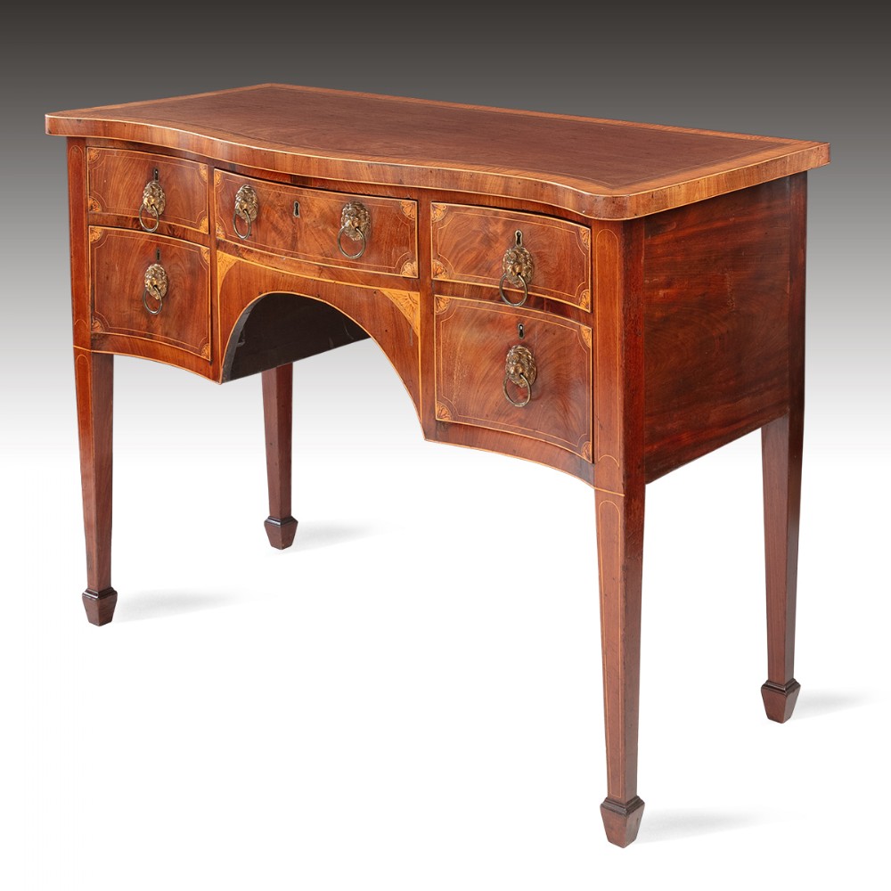 A George III mahogany sideboard featuring a serpentine front, inlaid drawer fronts with lion mask ring handles, and tapered square legs ending in spade feet.