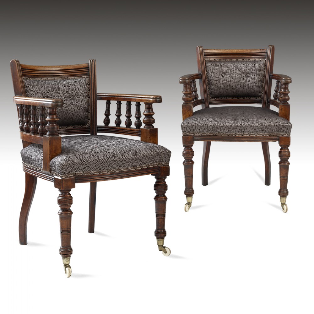 A pair of 19th-century mahogany desk armchairs featuring turned spindle supports, patterned fabric upholstery with stud trimming, and front turned legs on castors.