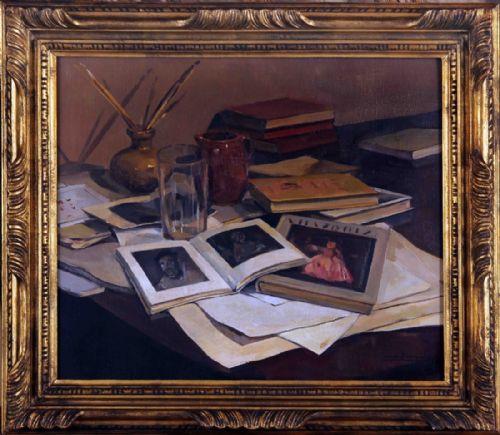 fig 1. An oil painting depicting an artist studio still life arrangement featuring open art books, loose papers, a glass tumbler, paintbrushes in a pot, and a terracotta jug.
