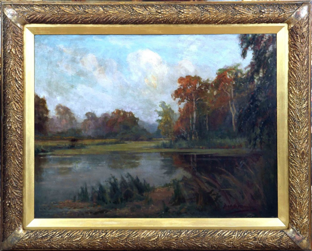 A framed oil painting depicting an autumnal lake landscape with orange trees and reflections on dark water, set within an ornate gilded frame.
