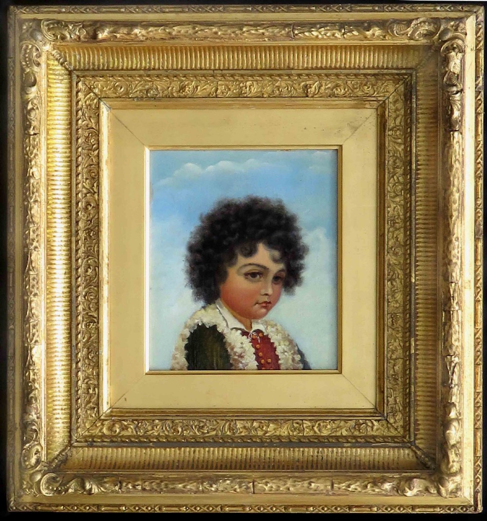 An oil portrait on board depicting a young boy with dark curly hair in traditional attire, framed in a heavily moulded gold gilt frame.