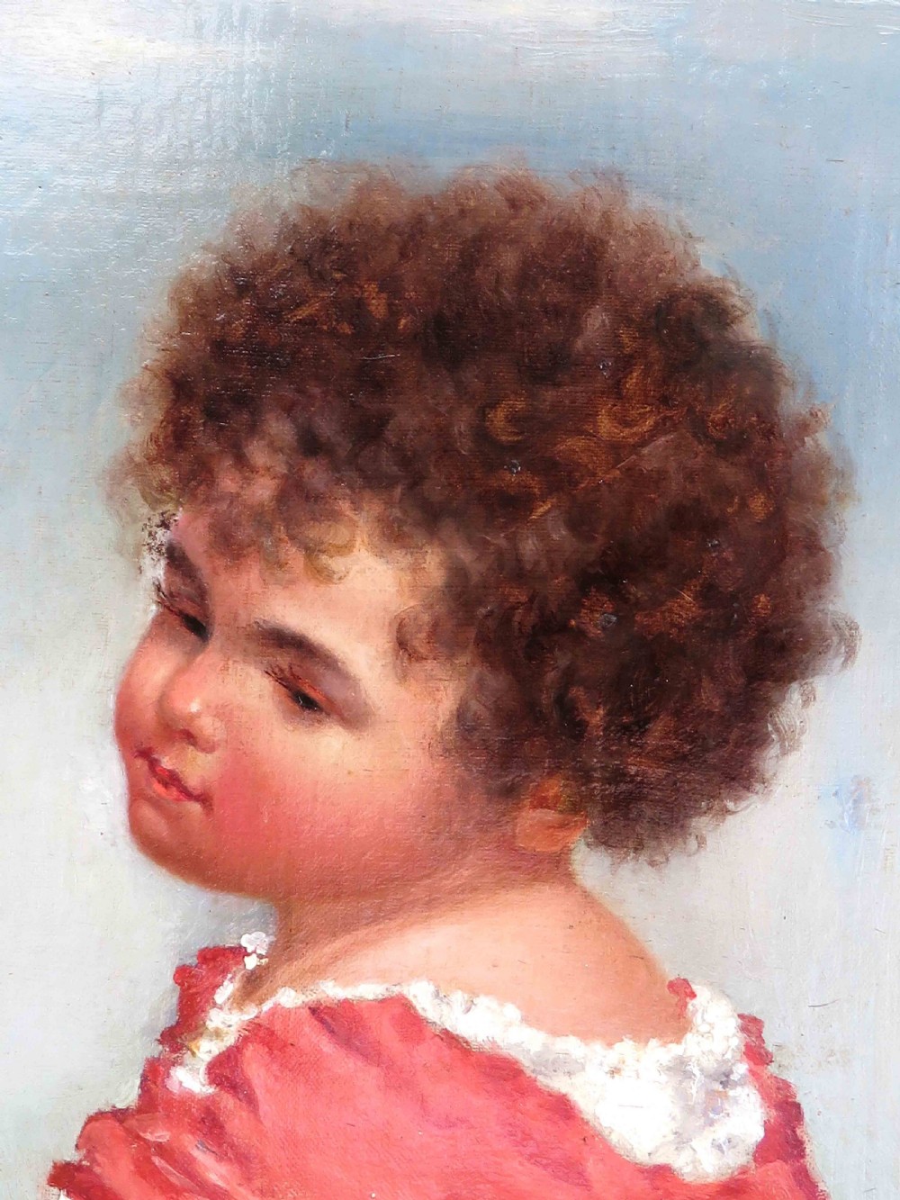 An oil portrait painting of a child with dark curly hair in a red garment, displayed inside a heavy gilt frame. View II