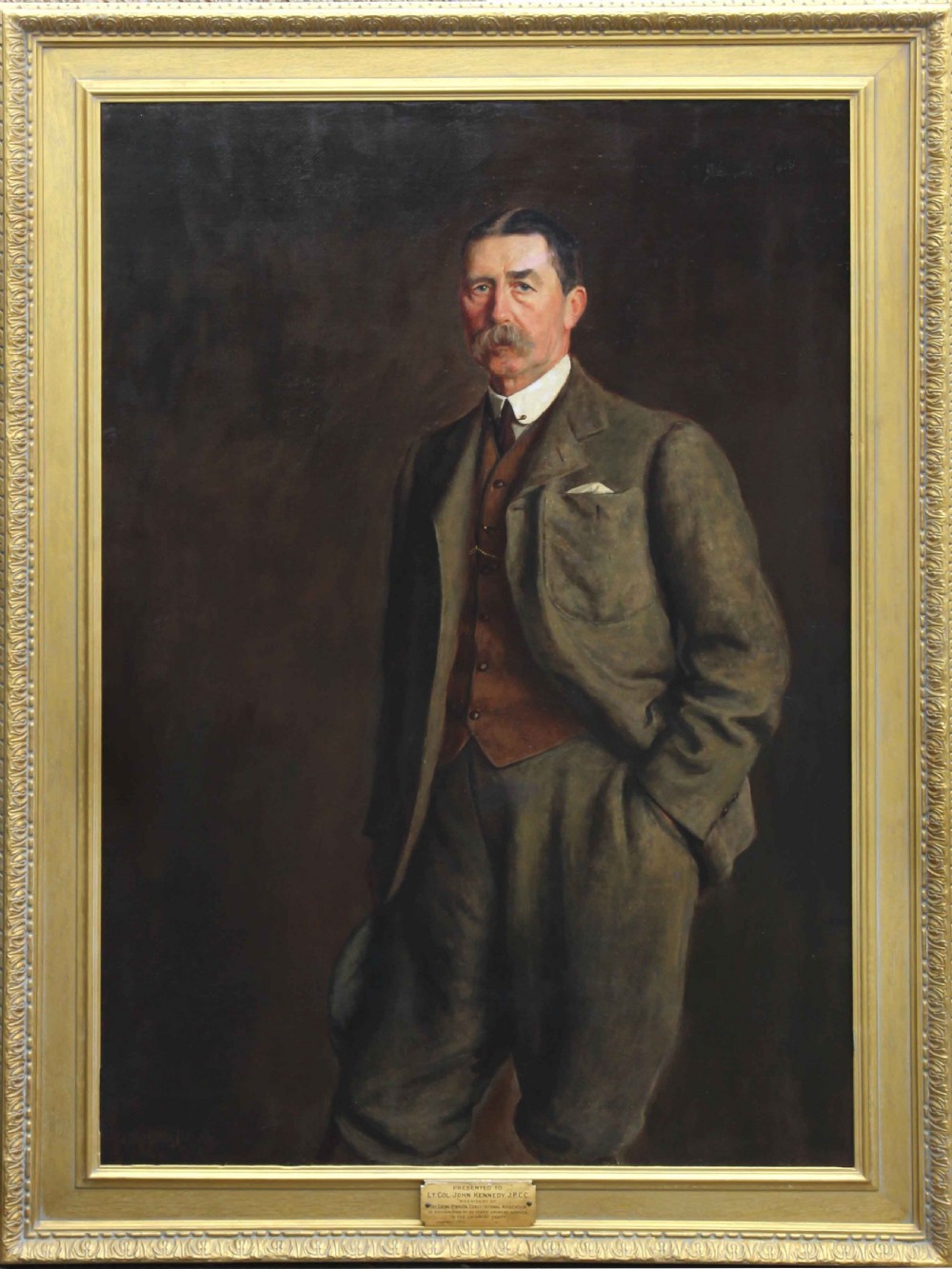 A large framed Edwardian oil portrait painting depicting a standing gentleman in a brown suit against a dark background.